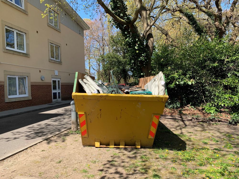 Yellow Dumpster Overflowing With Debris Sits on Grass Near a Building and Trees — Mount Isa Skips In Cloncurry, QLD