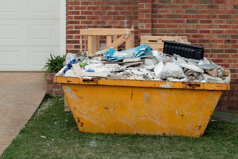 Yellow Dumpster Overflowing With Construction Debris, In Front Of A Brick Wall And Garage Door — Mount Isa Skips In Camooweal, QLD