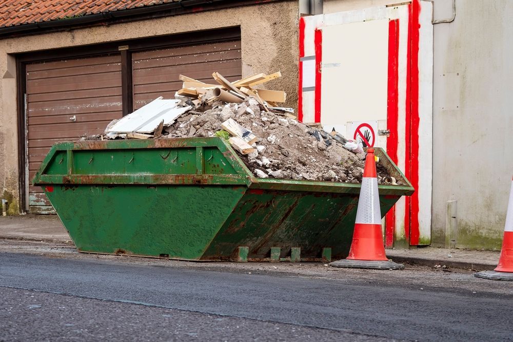 Green Dumpster Overflowing With Construction Debris On A City Street, With Safety Cones Nearby — Mount Isa Skips In Camooweal, QLD