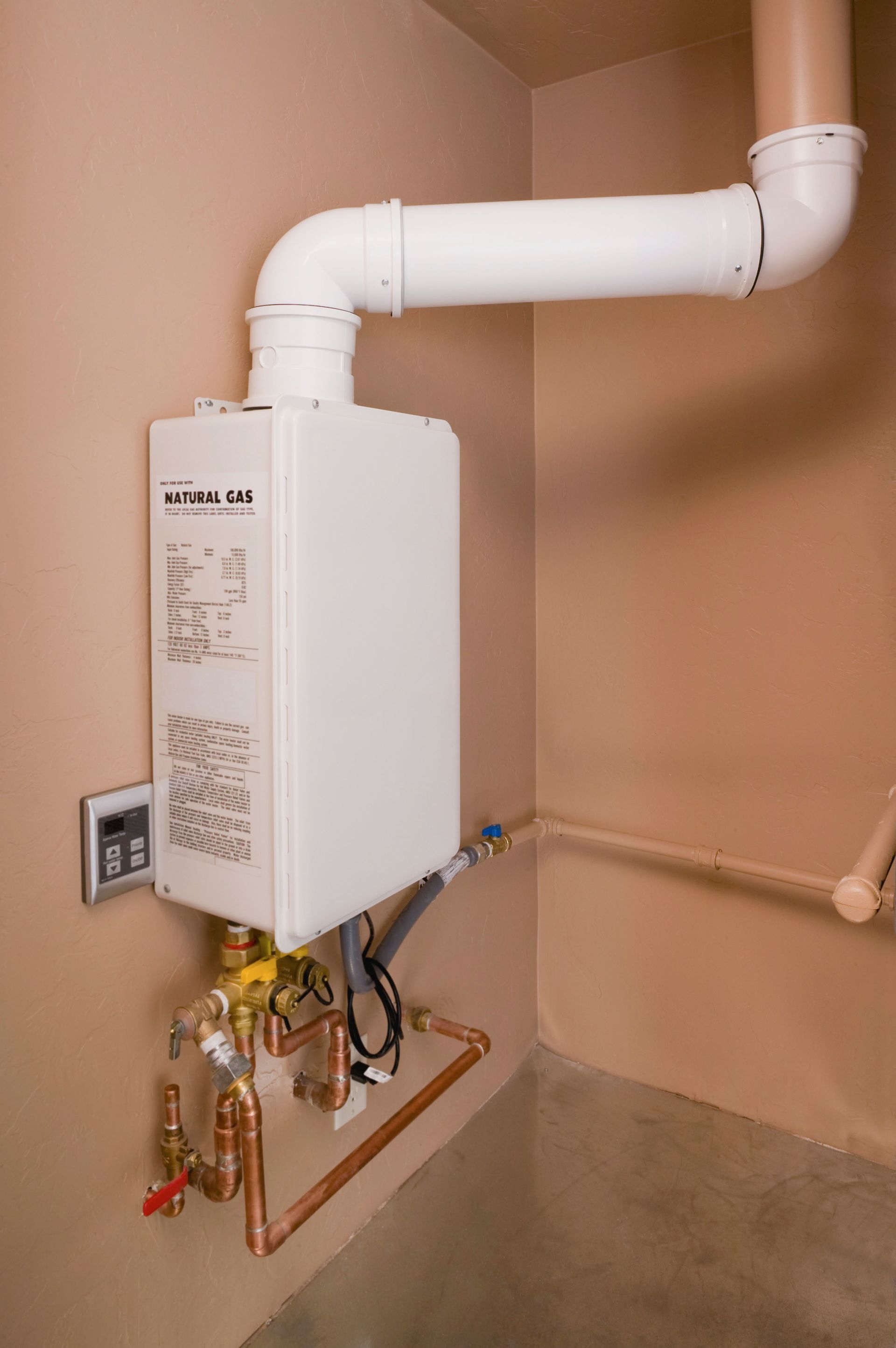 Wall-mounted white water heater with pipes and valves in a utility closet.