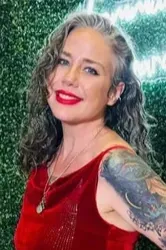 Smiling person in a red velvet dress with a tattooed arm against a green textured background
