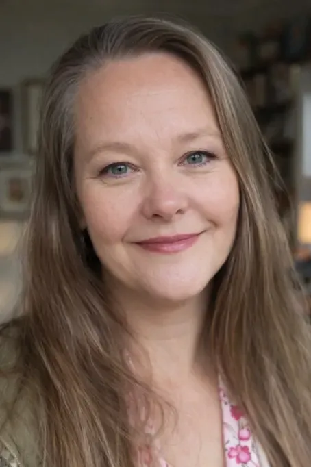 Portrait of a smiling woman with long light brown hair against a softly blurred indoor background