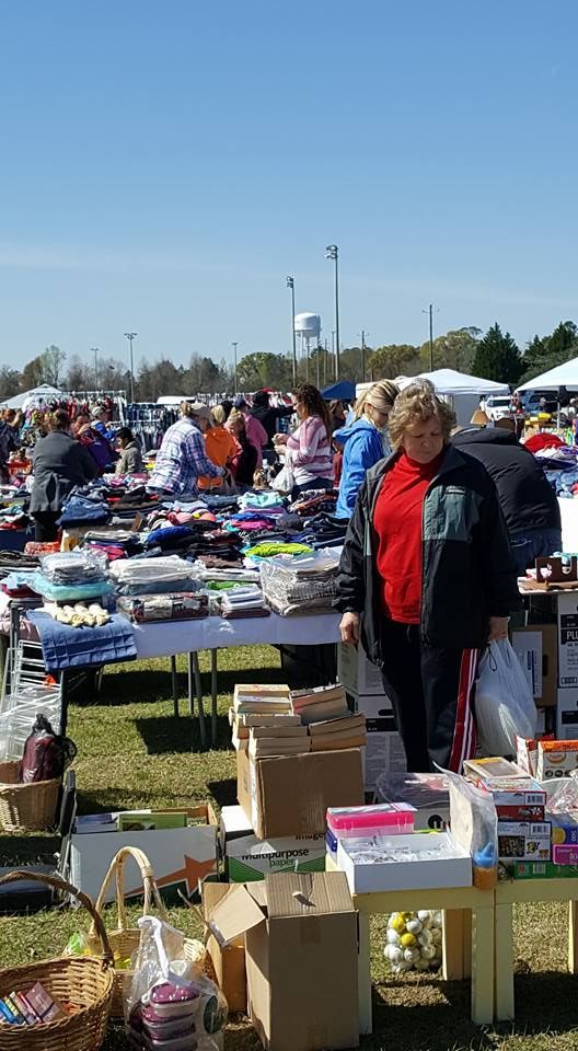 Outdoor flea market with tables of secondhand goods and shoppers browsing under a clear blue sky