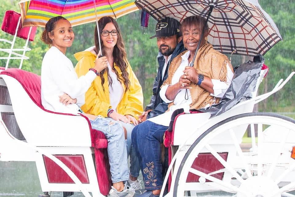 Four people sit on a white cart under colorful umbrellas, smiling outdoors.