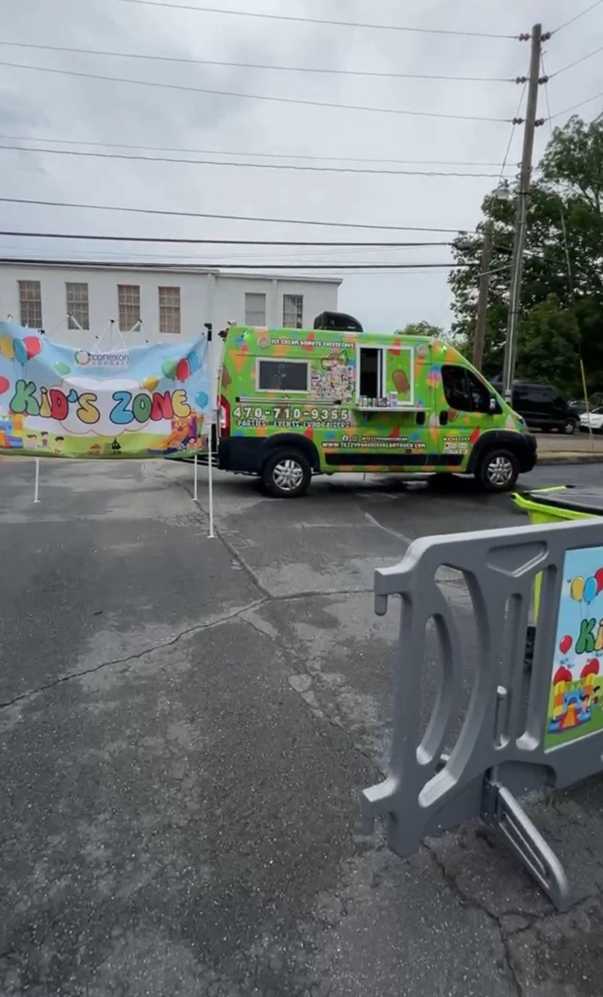 Colorful decorated food truck parked beside a banner in a wet lot, with barriers in the foreground.