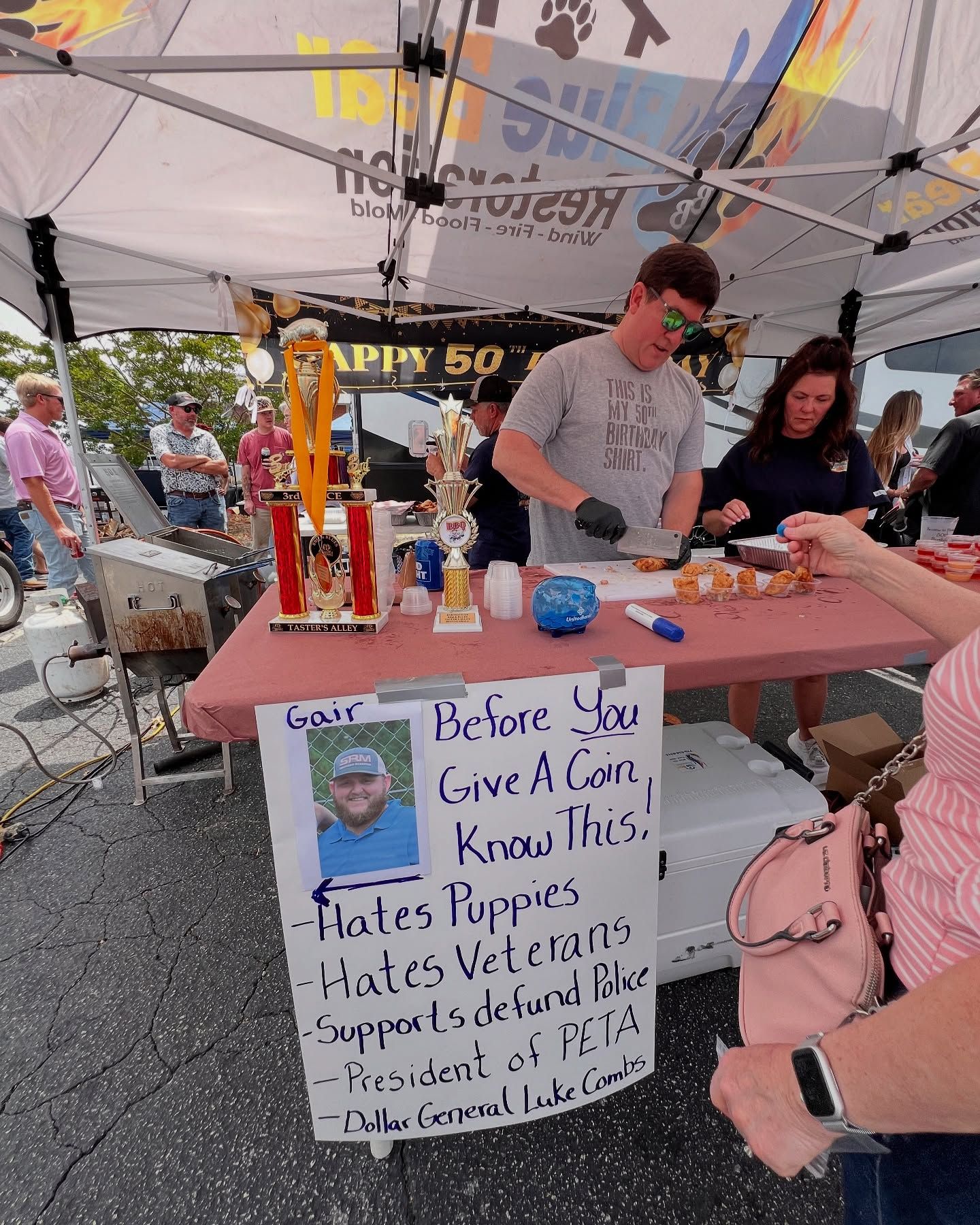 People at a protest table under a canopy with a handwritten sign and candles.