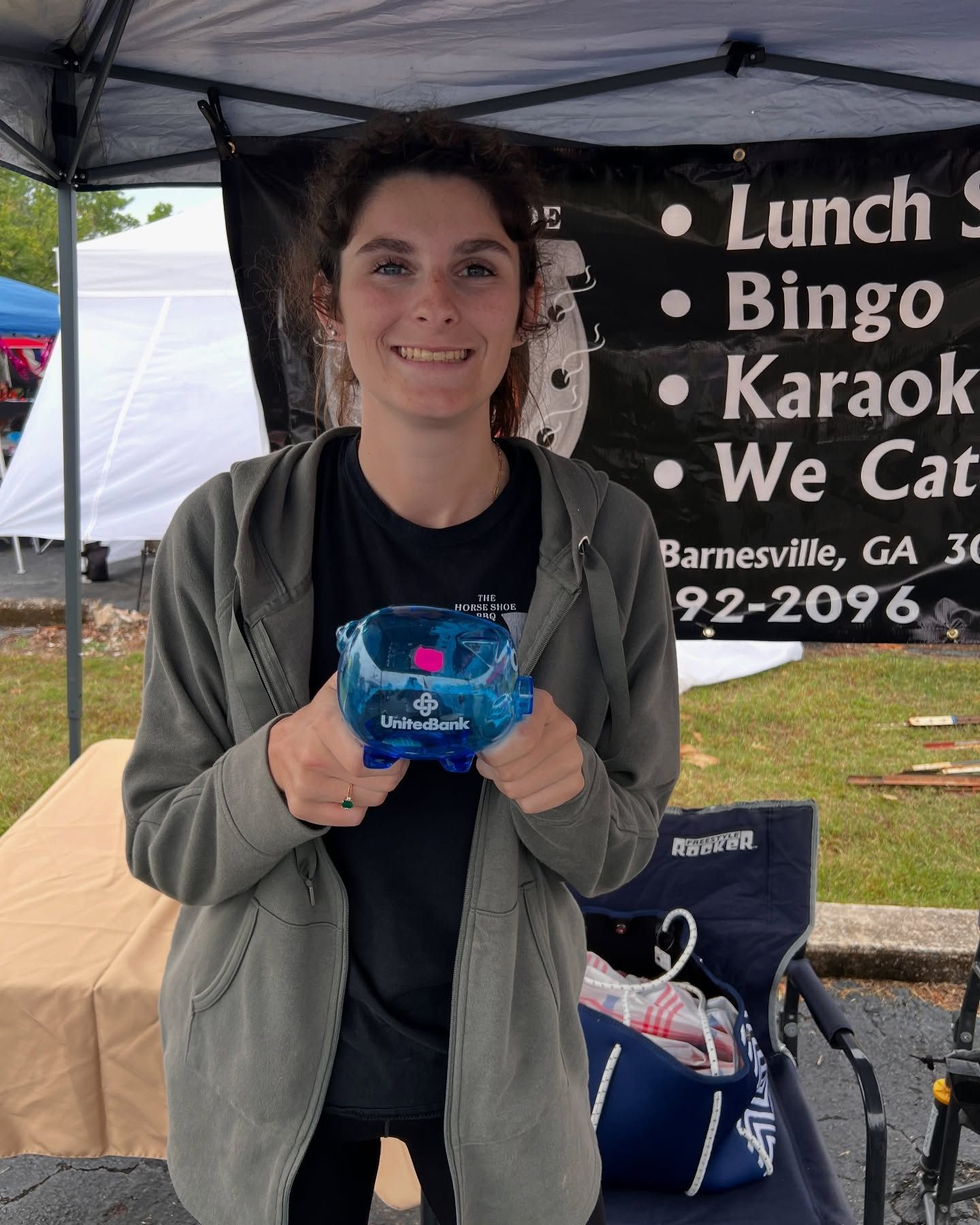 Person holding a blue award under a canopy at an outdoor event booth with a menu sign behind.