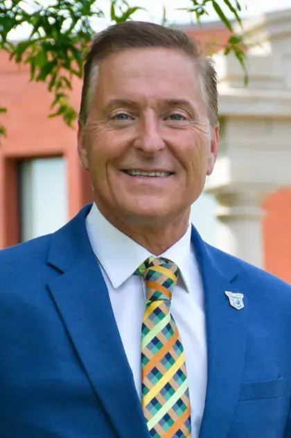 Smiling man in a blue suit with a patterned tie standing outdoors near a building