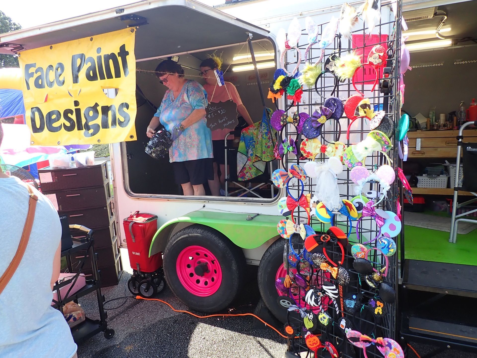Face painting booth with colorful display and two people under a canopy at a fair