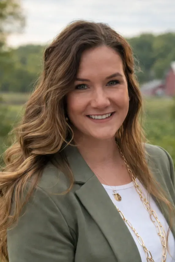 Smiling person in a green jacket outdoors with a blurred grassy background