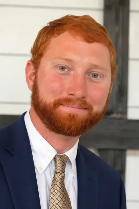 Portrait of a smiling red-haired man in a navy suit and patterned tie indoors
