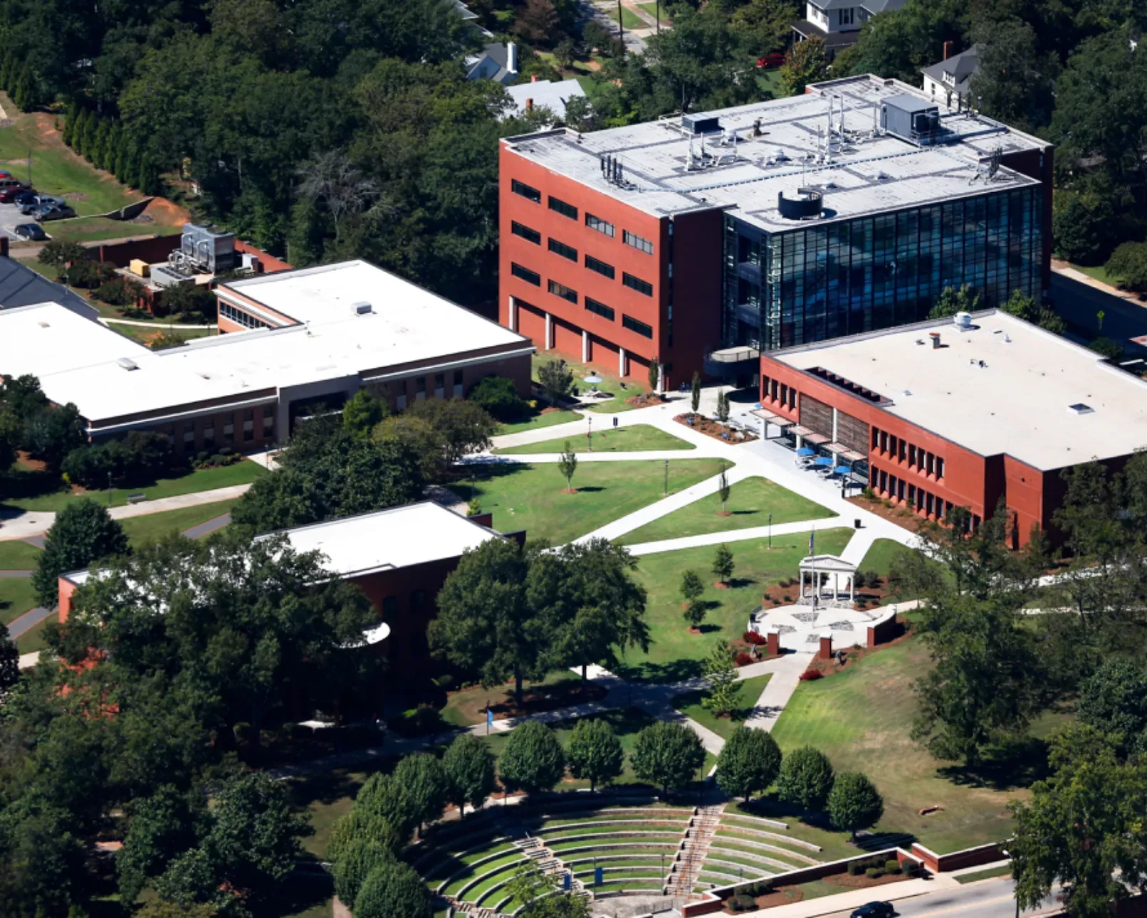 Aerial view of a red-brick and glass campus building beside lawns, walkways, and trees.
