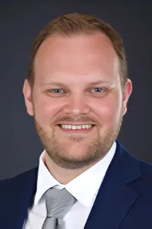 Smiling man in a navy suit and gray tie against a dark studio background