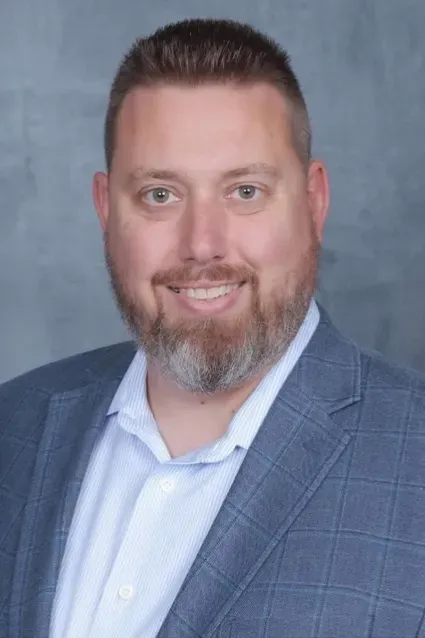 Portrait of a smiling man in a blue suit jacket and white shirt against a gray backdrop