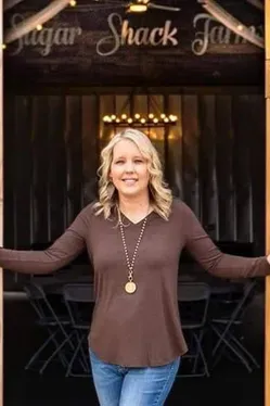 Woman standing in front of a Sugar Shack sign, smiling with arms outstretched.