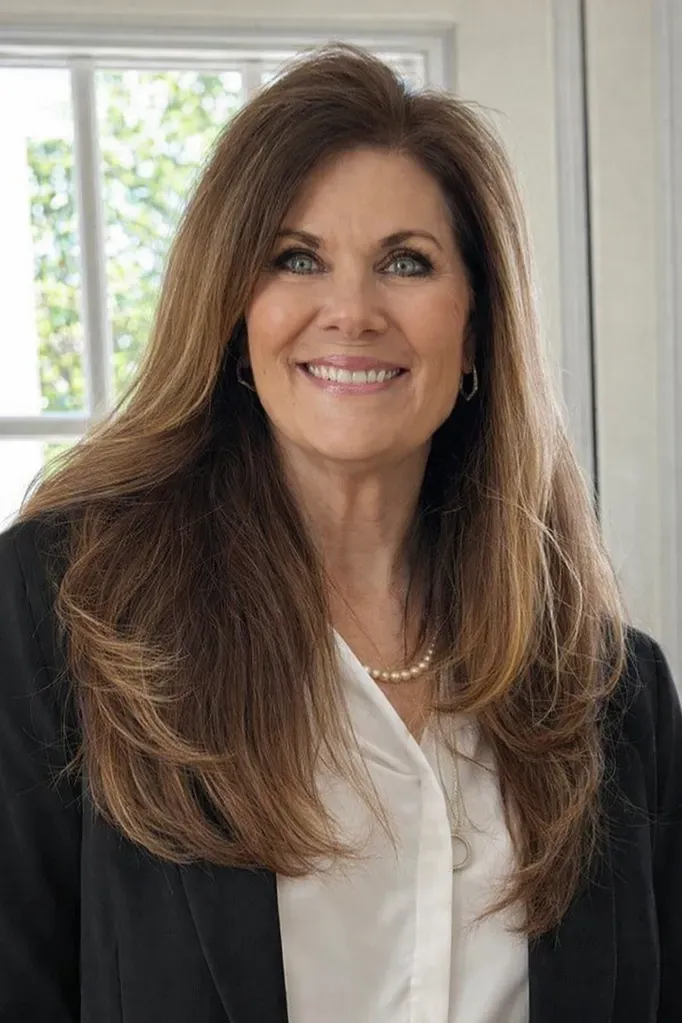 Portrait of a smiling woman in a black blazer and white blouse by a window