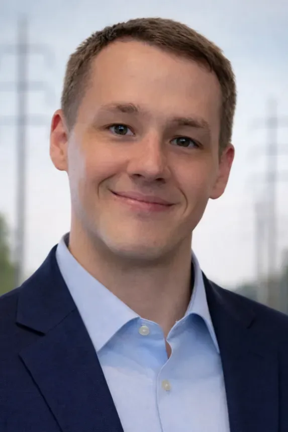 Portrait of a smiling person in a navy blazer and light blue shirt against a blurred office background