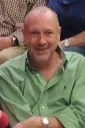 Smiling man in a green shirt sitting indoors with arms crossed