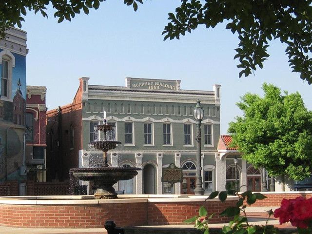 Historic town square with a fountain, brick buildings, and trees under a clear blue sky