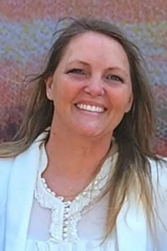 Smiling woman in a white blouse standing against a colorful wall