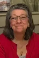 Smiling person with glasses and shoulder-length gray hair wearing a red top indoors