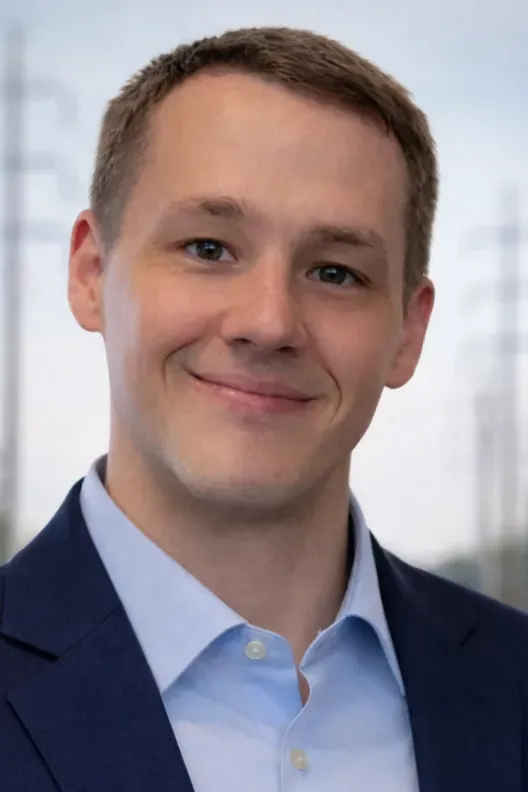 Smiling person in a navy blazer and light blue shirt against a blurred indoor background