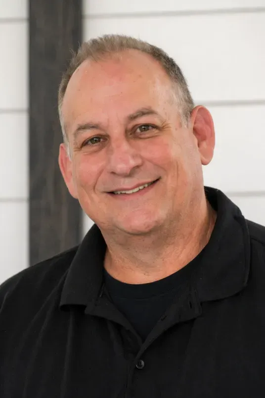 Smiling man in a black shirt standing indoors against a light wall