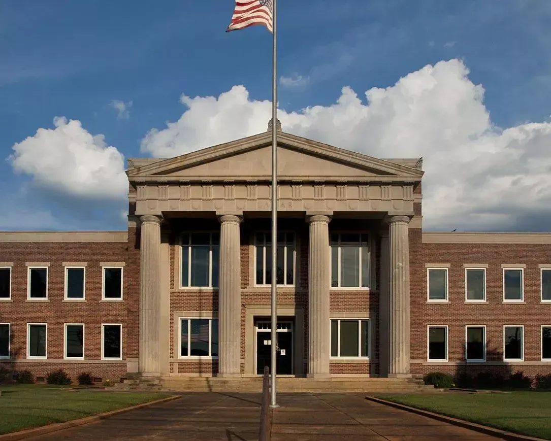Historic brick building with tall white columns and an American flag against a blue sky