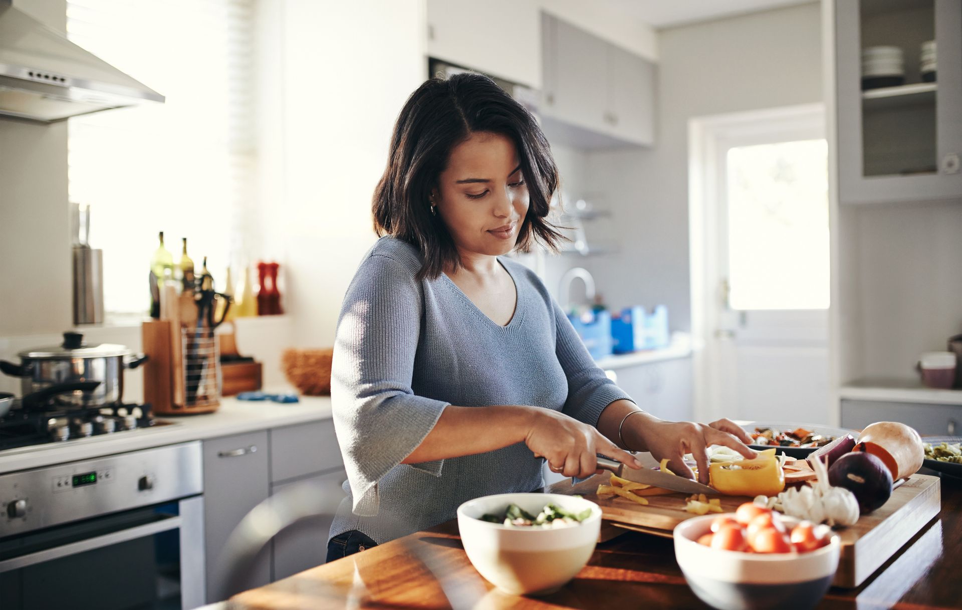 A woman is cutting vegetables on a cutting board in a kitchen.