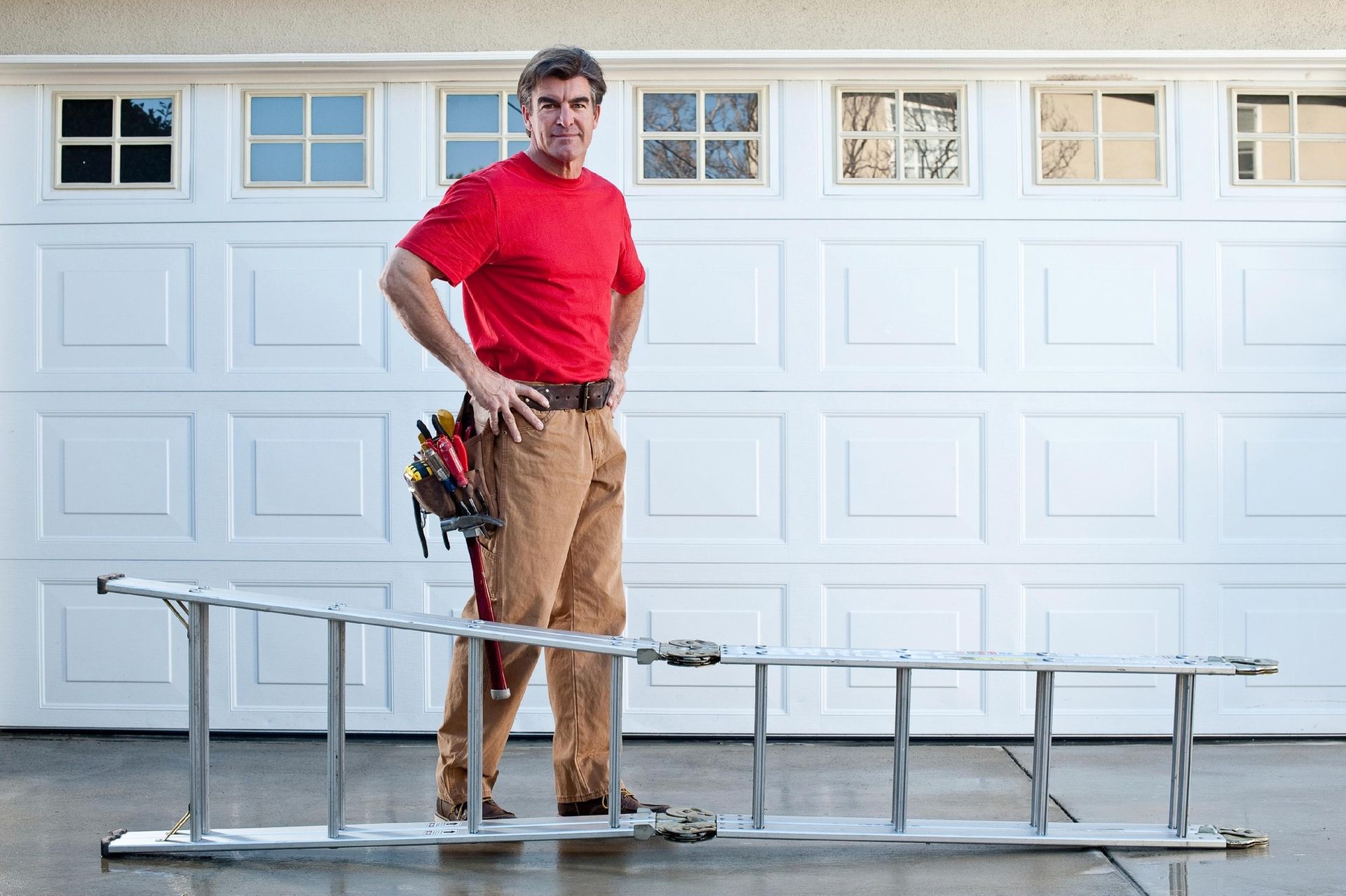 A man is standing next to a ladder in front of a garage door.