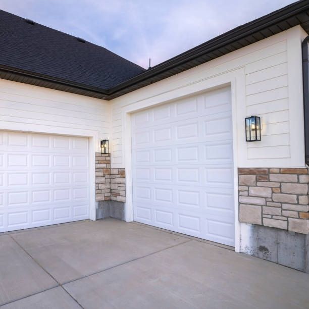 A white house with two garage doors and a stone wall