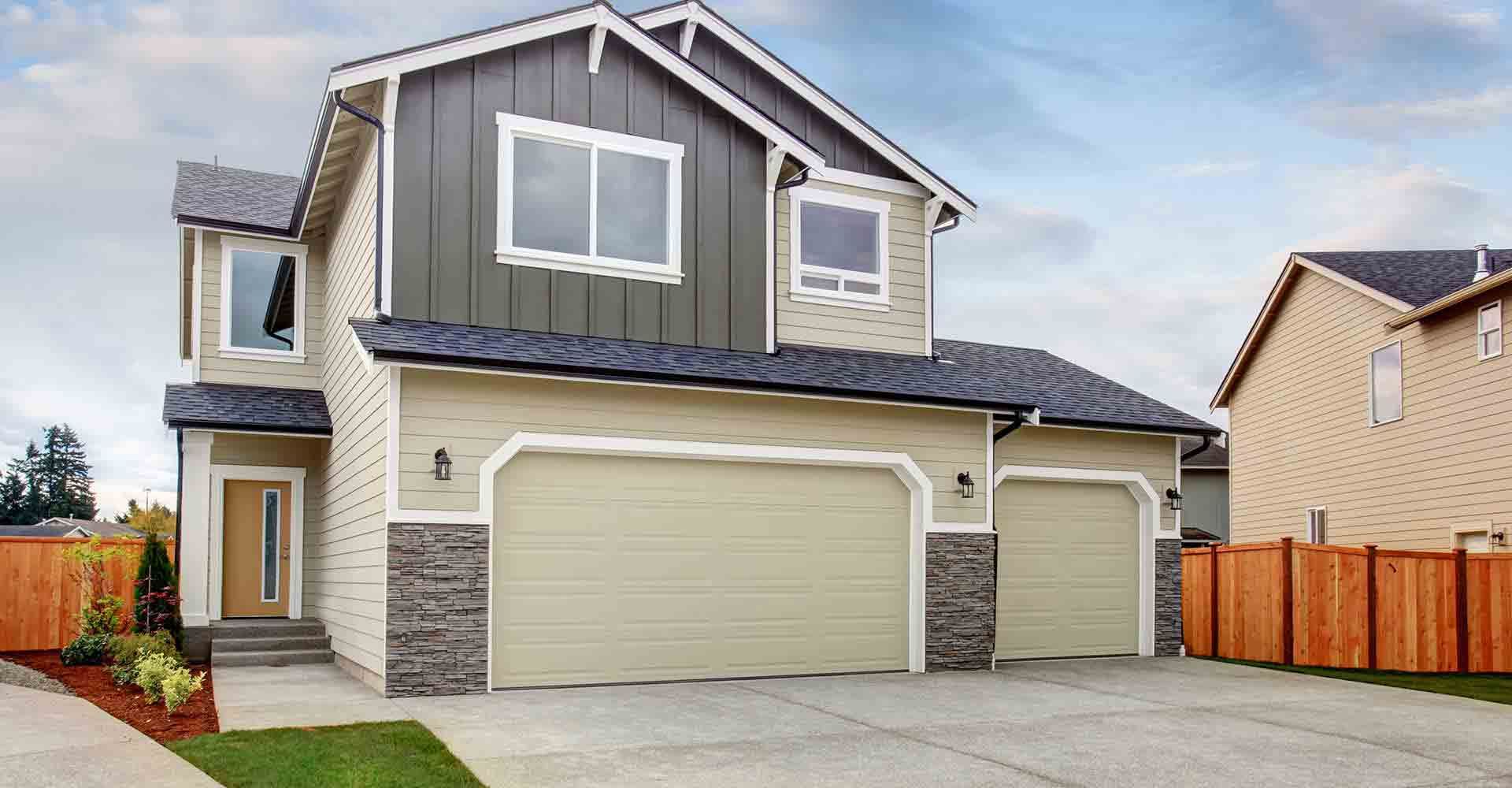 A large house with two garage doors and a wooden fence in front of it.