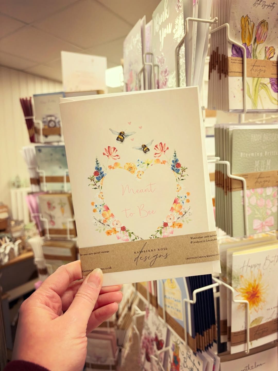 Hand holding a greeting card with floral heart design in a shop.
