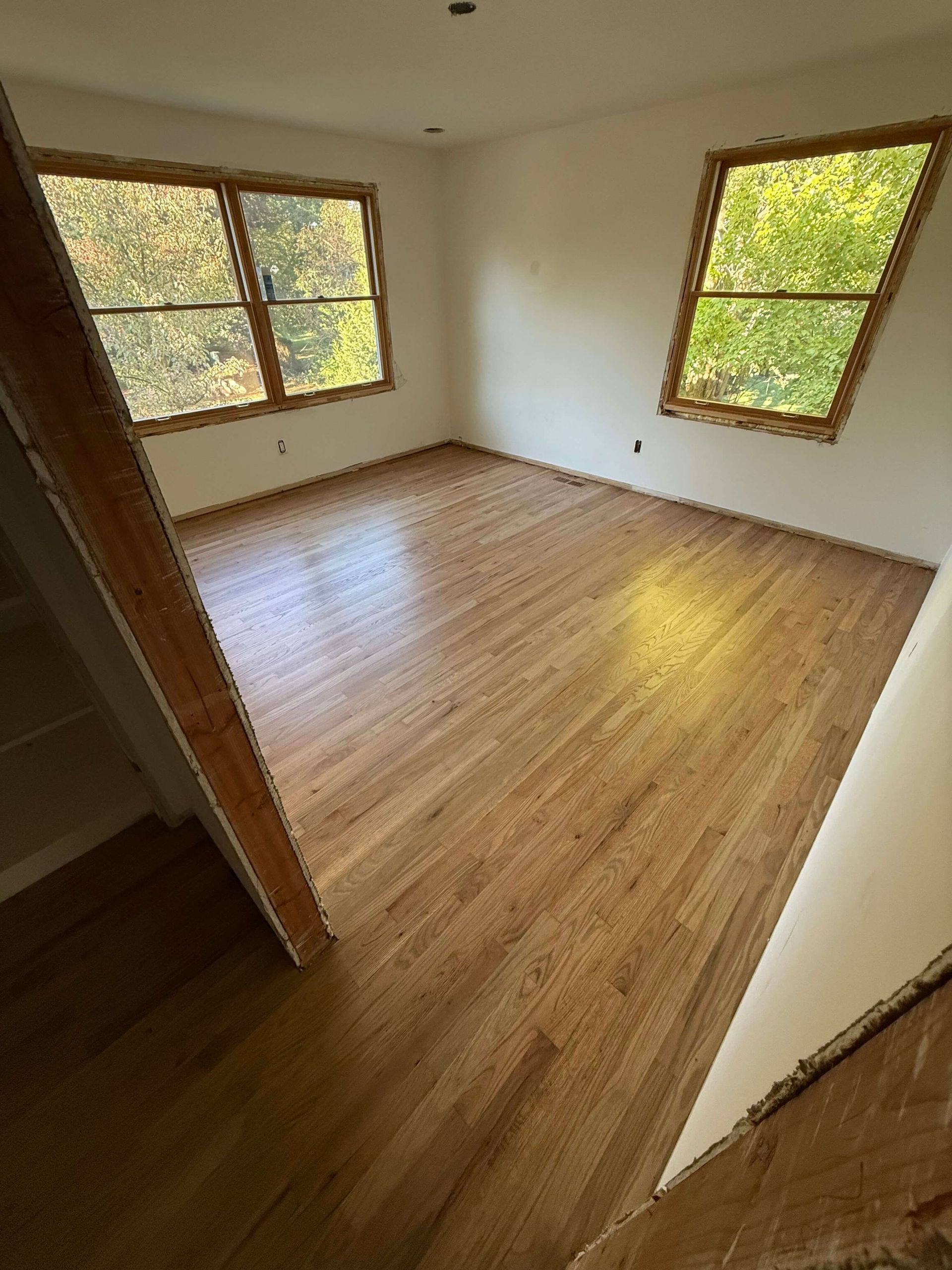 Sunlit room with hardwood floors and two windows with blinds