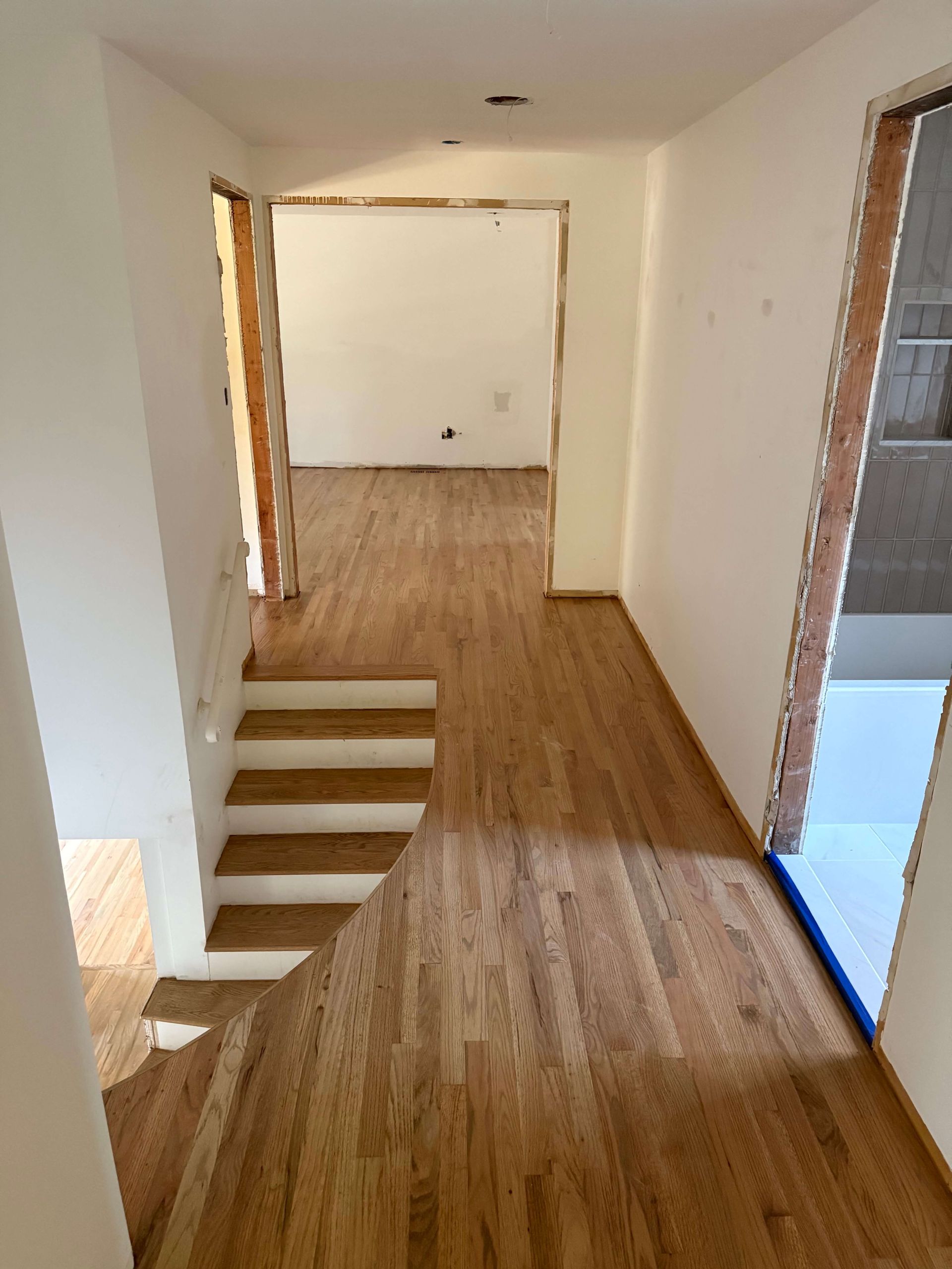 Narrow hallway with wood flooring, open doorways, and a small step-down staircase on the left.