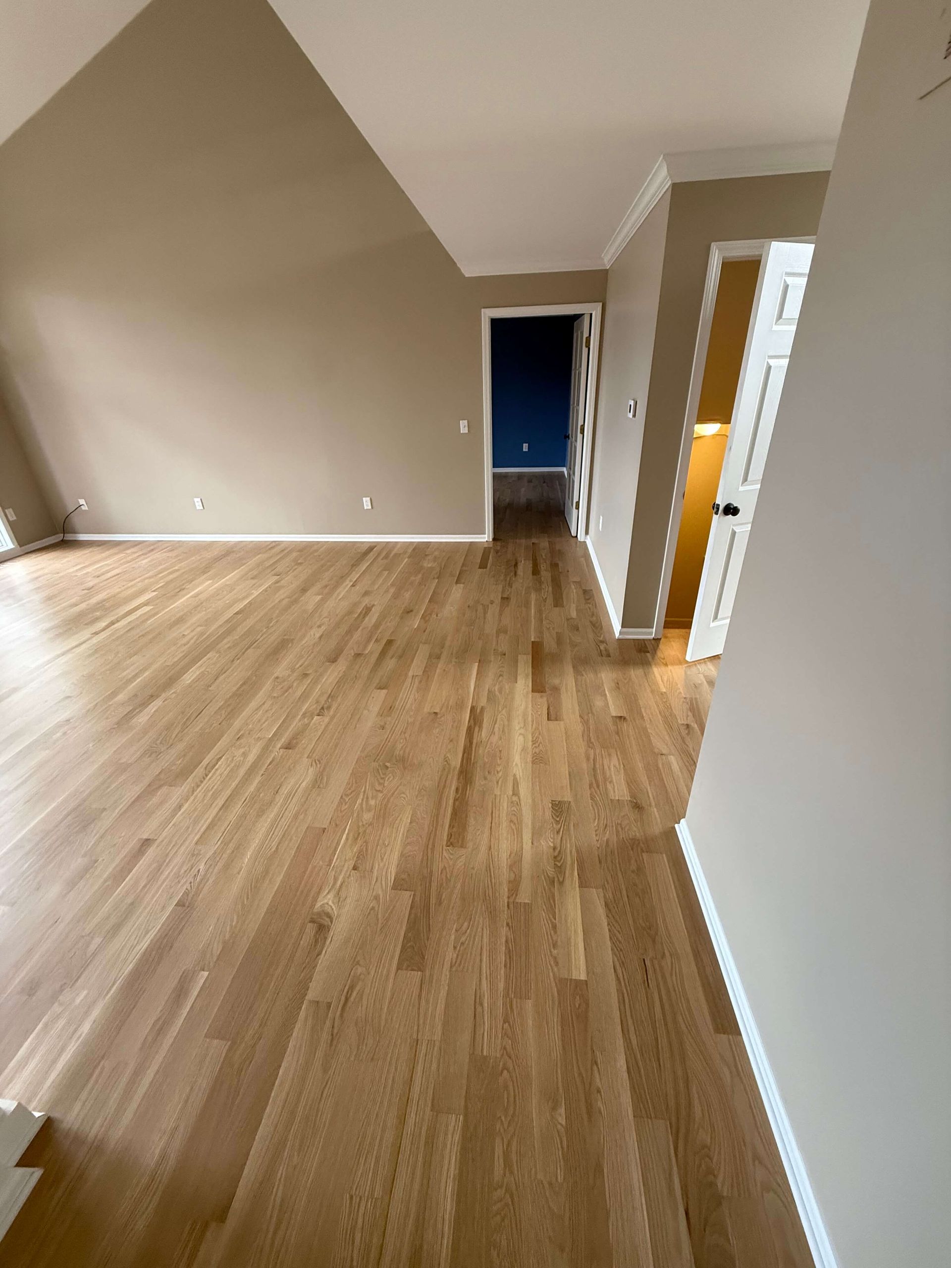 Room with hardwood floors, beige walls, and a doorway leading to a lit hallway