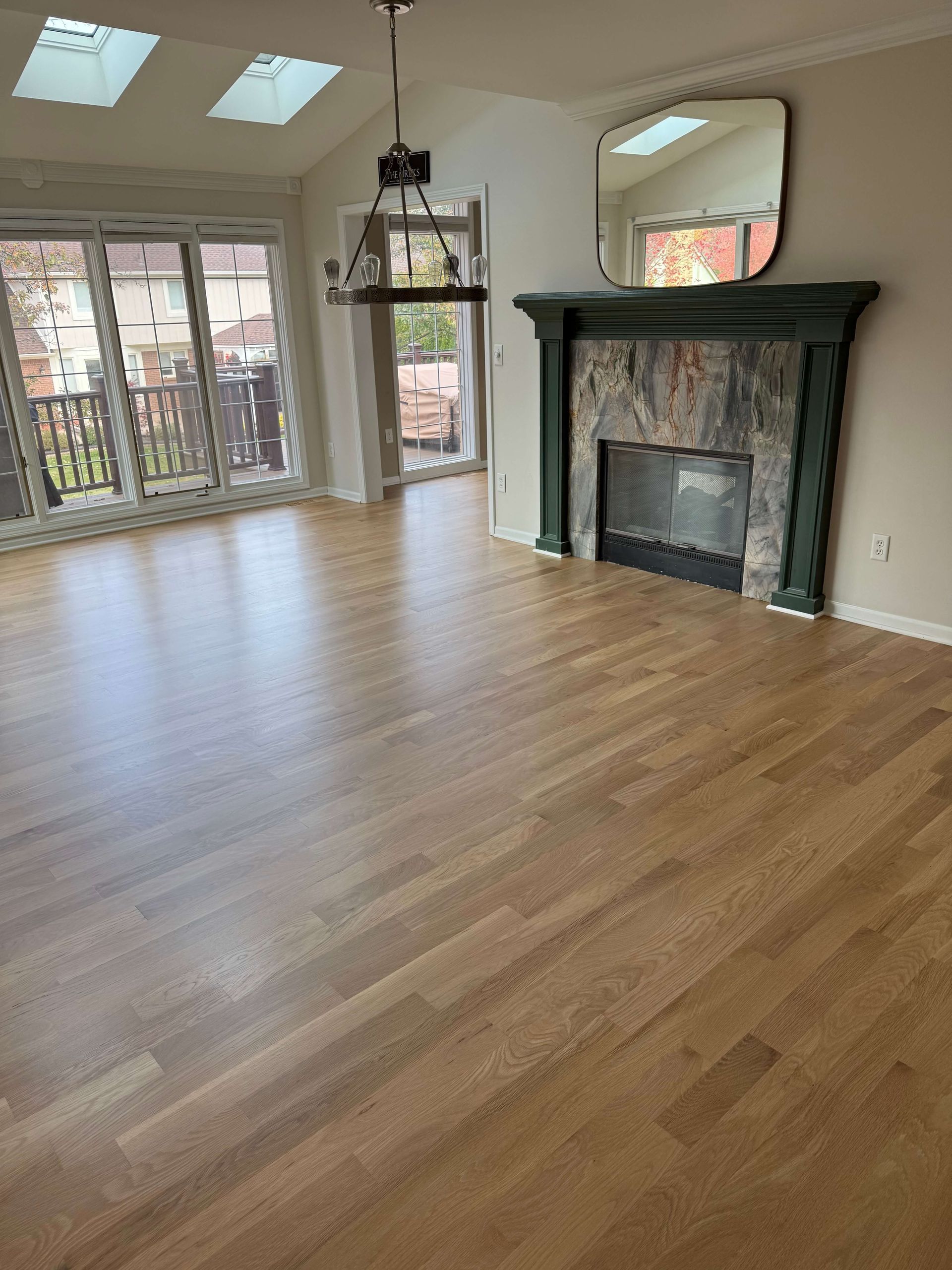 Living room with hardwood floors, large windows, and a dark green fireplace mantel