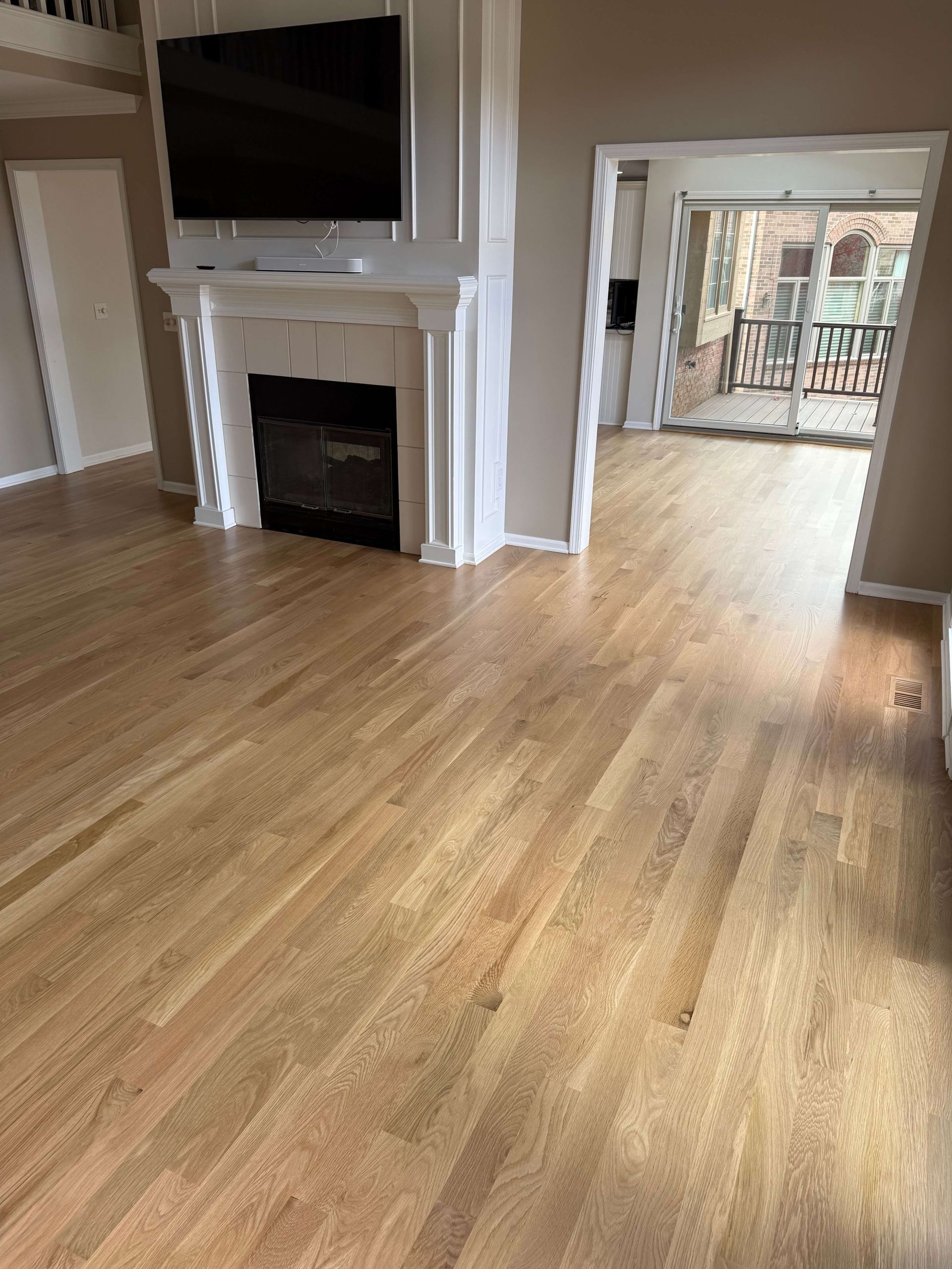 Living room with hardwood floors, fireplace, TV, and open doorway to a balcony.