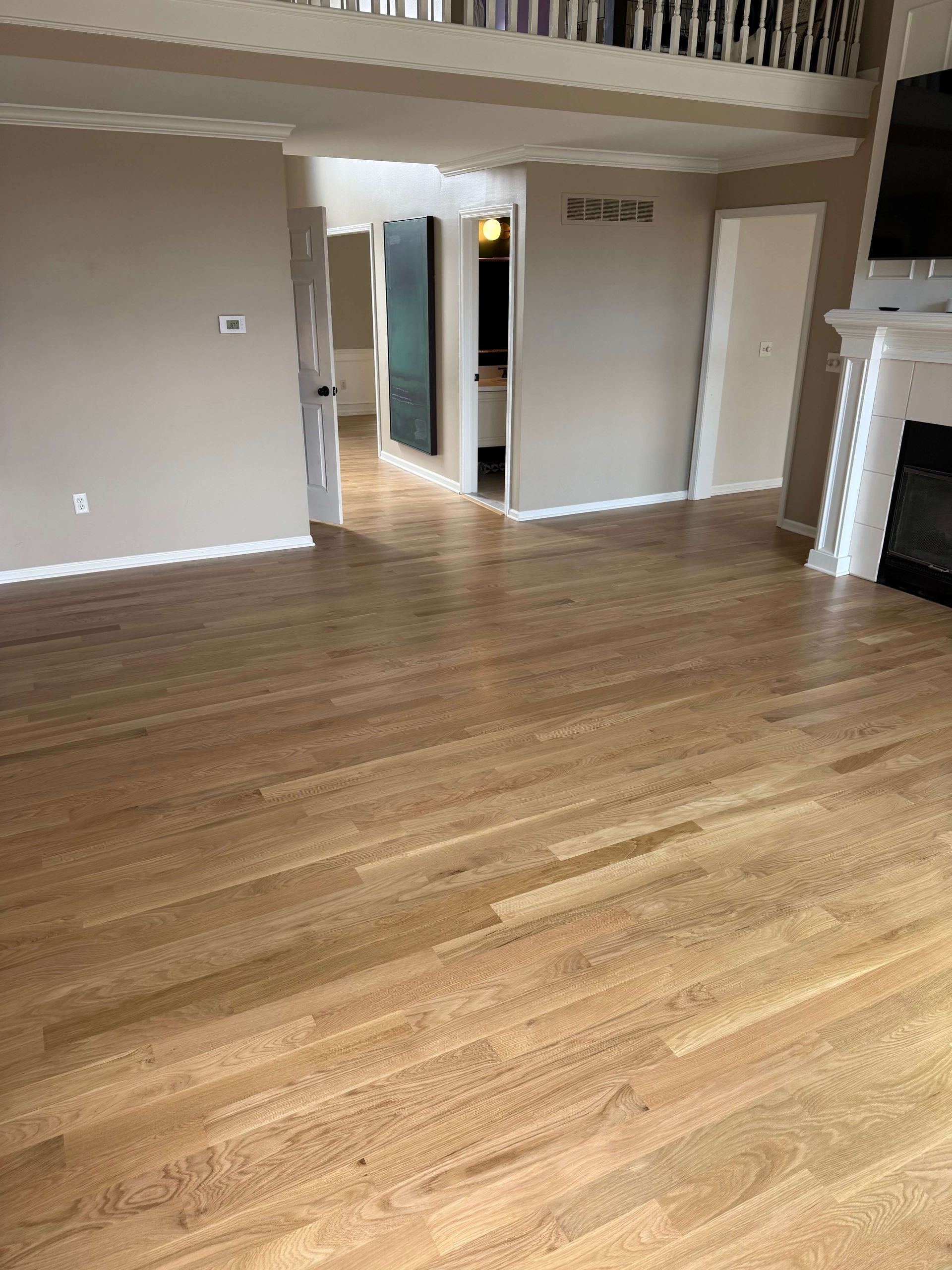 Hardwood living room with beige walls, loft railing, and doorway to a lit hallway