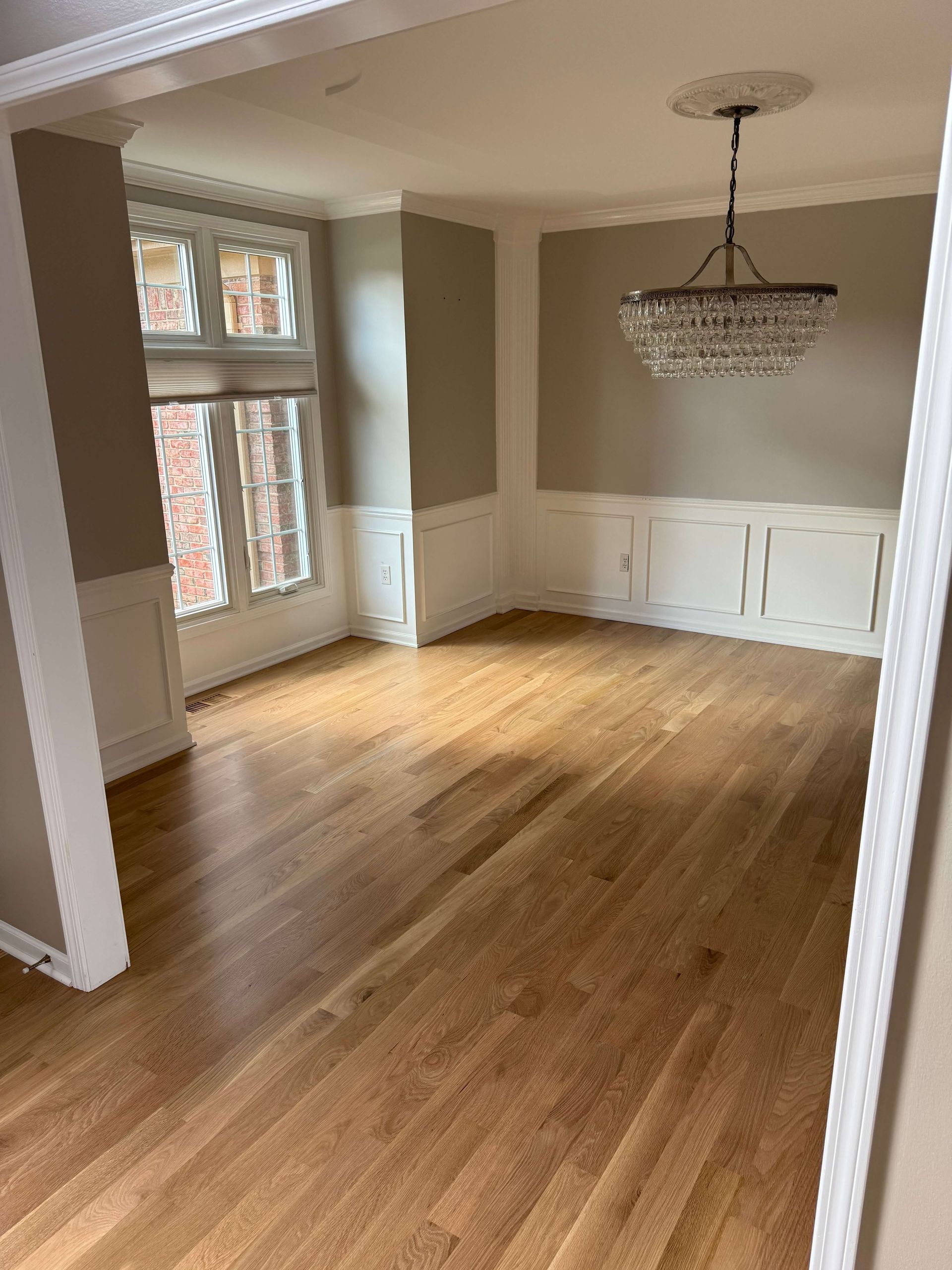 Dining room with hardwood floors, white wainscoting, and a chandelier near tall windows.