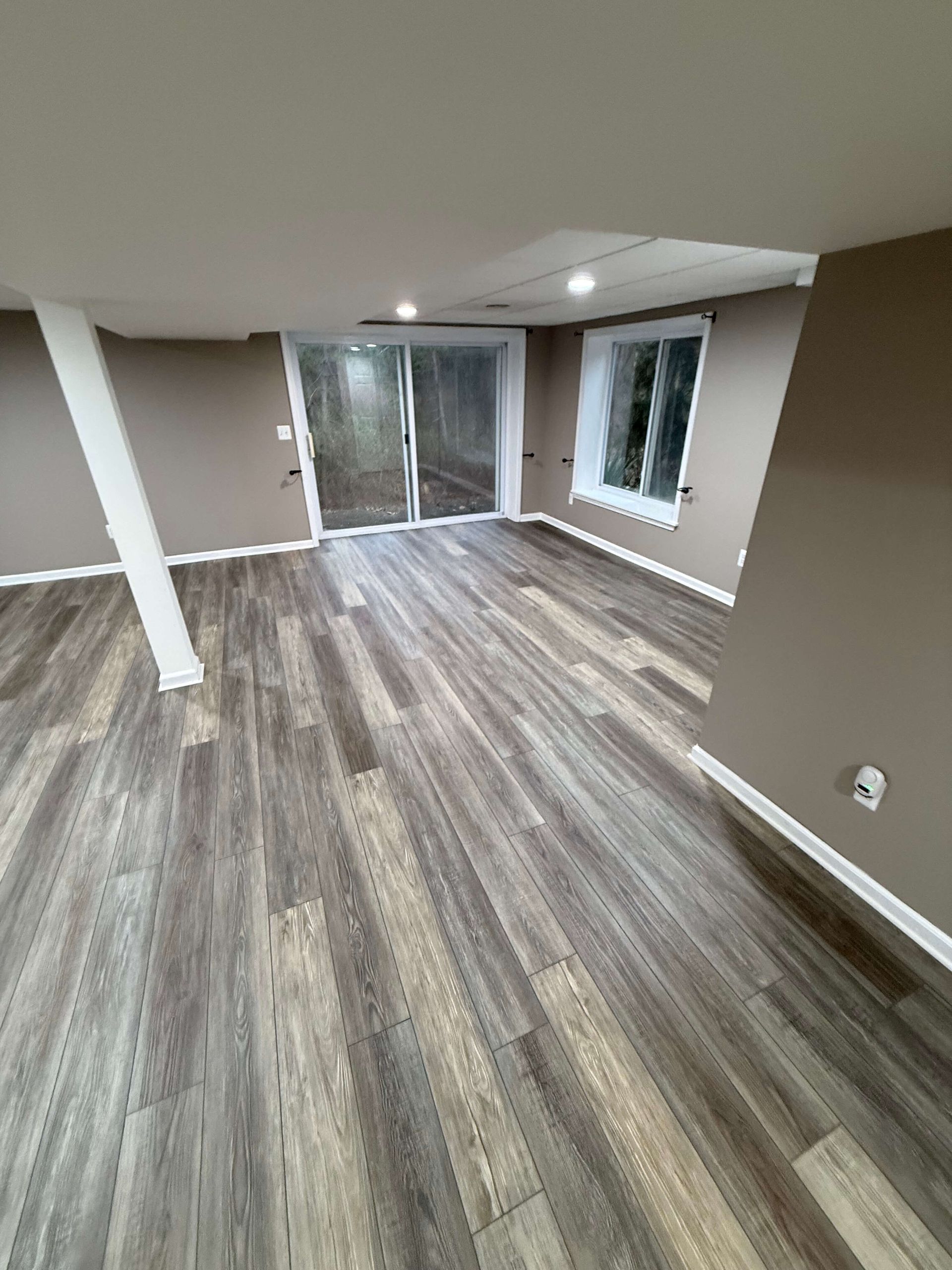 living room with gray wood floors, beige walls, white column, and sliding glass doors opening to outside.