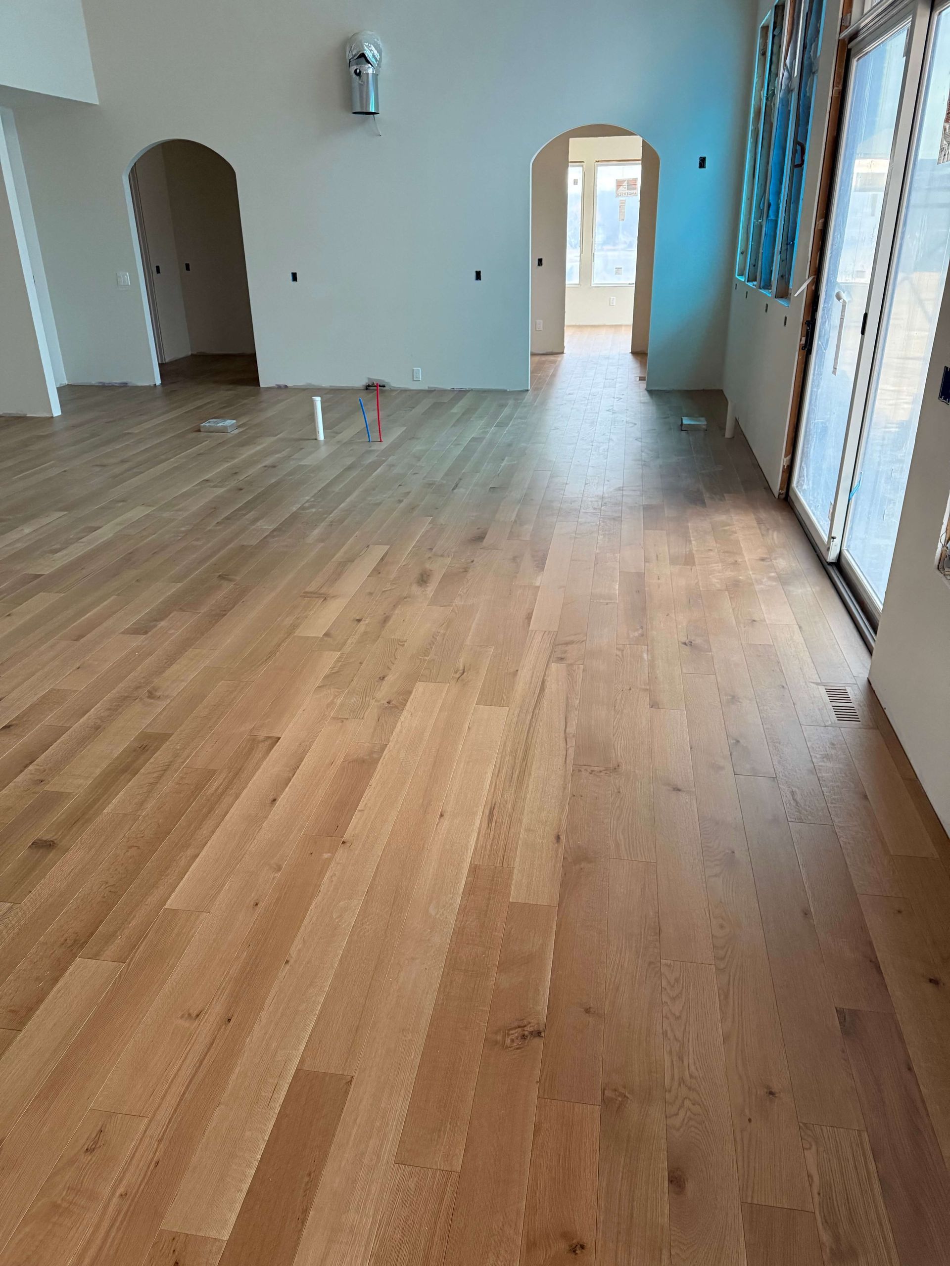 Empty room with light wood floors, white walls, arched doorways, and large windows on the right.