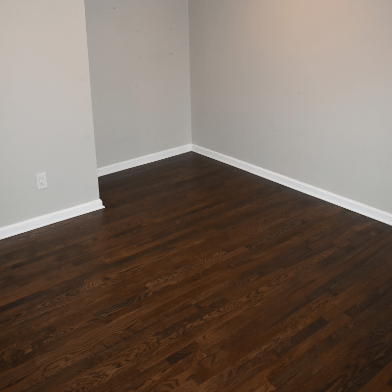 Room corner with gray walls, white baseboards, and dark wood flooring