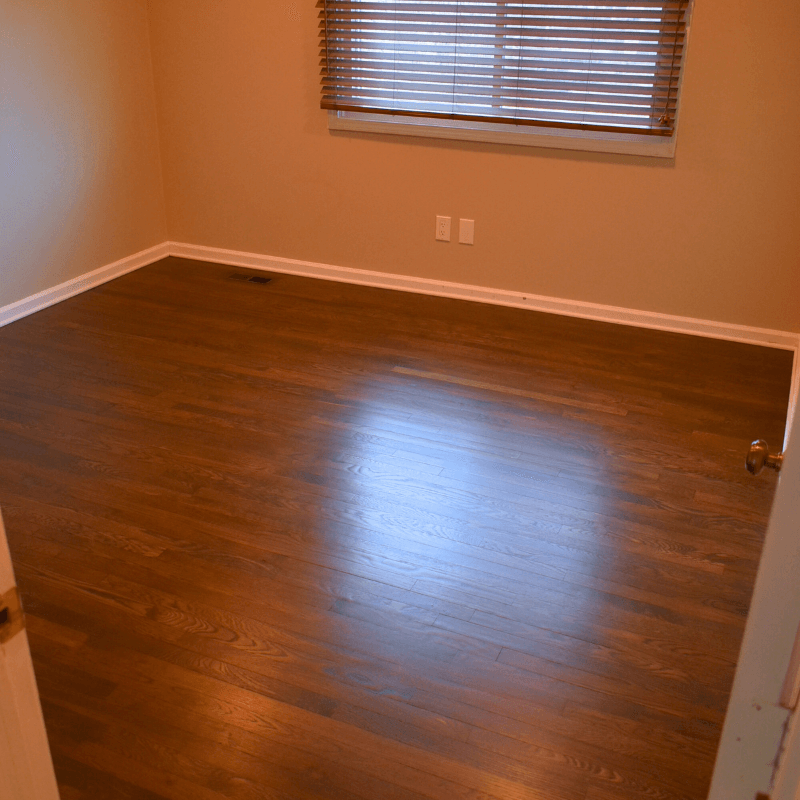 Room with dark hardwood floors, beige walls, and a window with blinds.