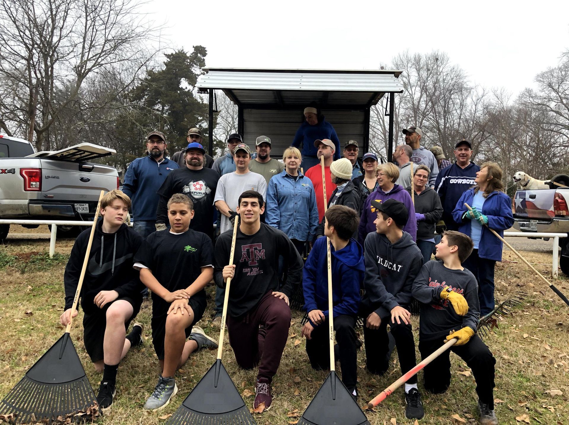 A group of people are standing in front of a truck holding rakes.