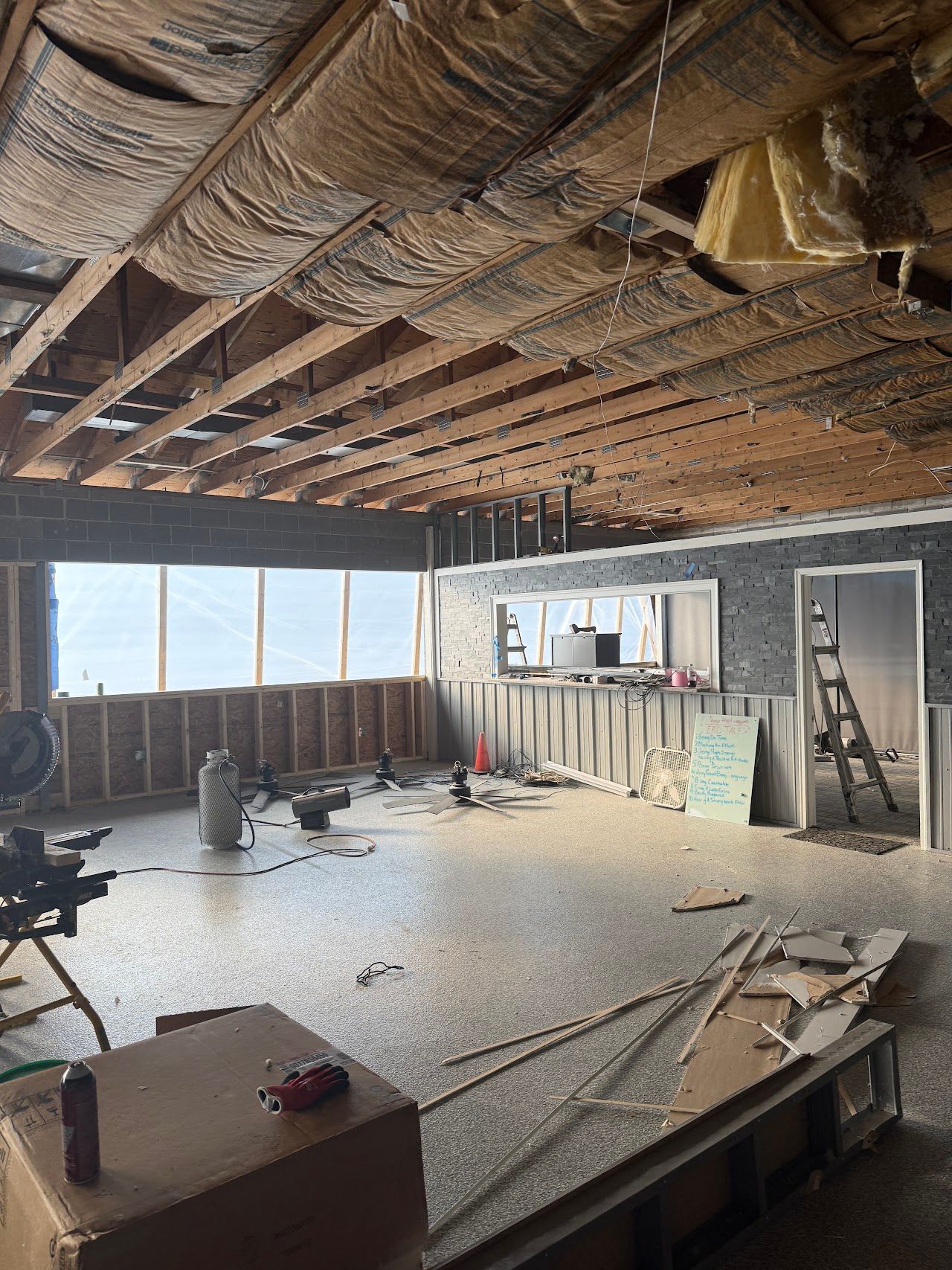 Building interior with exposed ceiling framing, insulation, and restoration equipment.