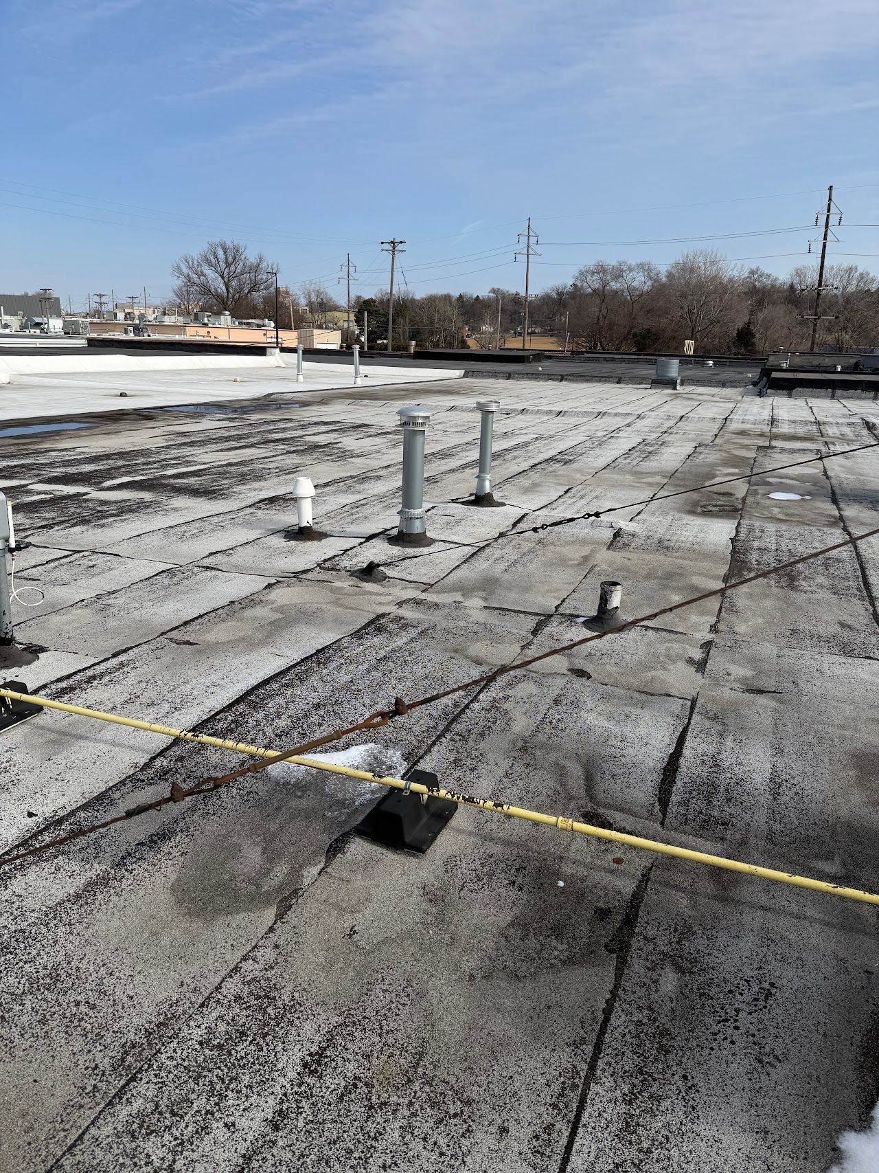 Low-slope roof surface with seams, penetrations, and rooftop piping.