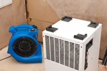 Blue and white portable air mover and dehumidifier against a wall in a room