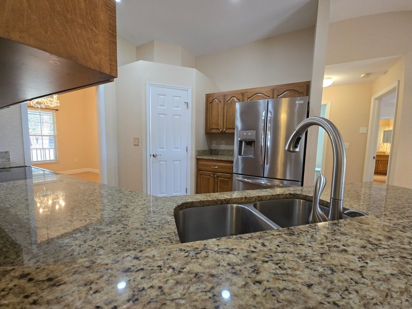 Kitchen with granite countertop, double sink, and stainless steel refrigerator in a bright home interior