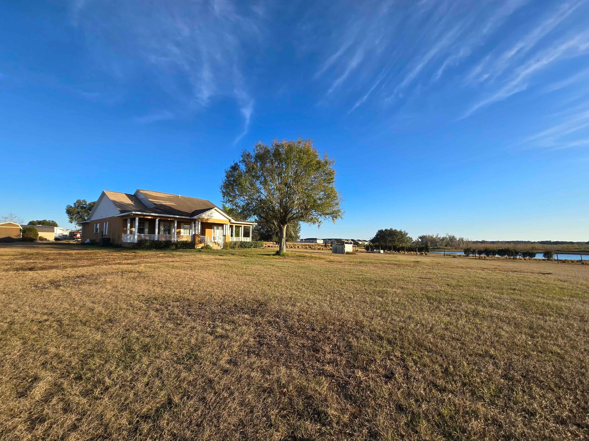 Rural farmhouse beside a large tree under a bright blue sky, overlooking an open field